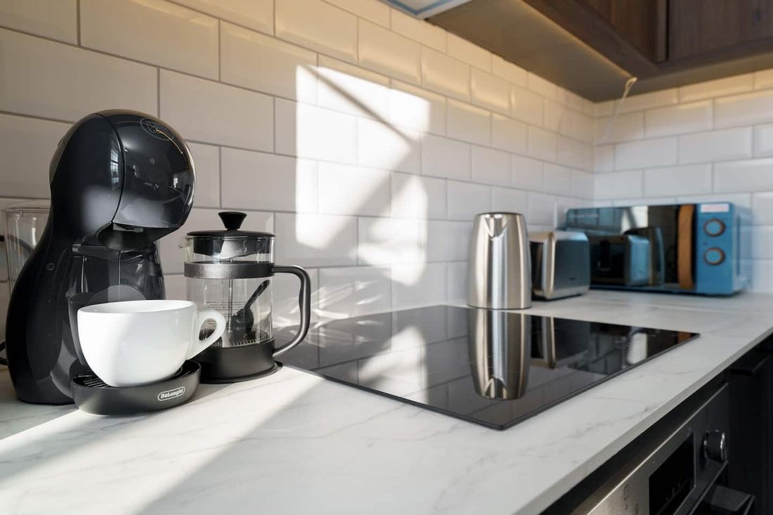 Coffee machine, cup and cafetière set out on a marble kitchen worktop in morning light
