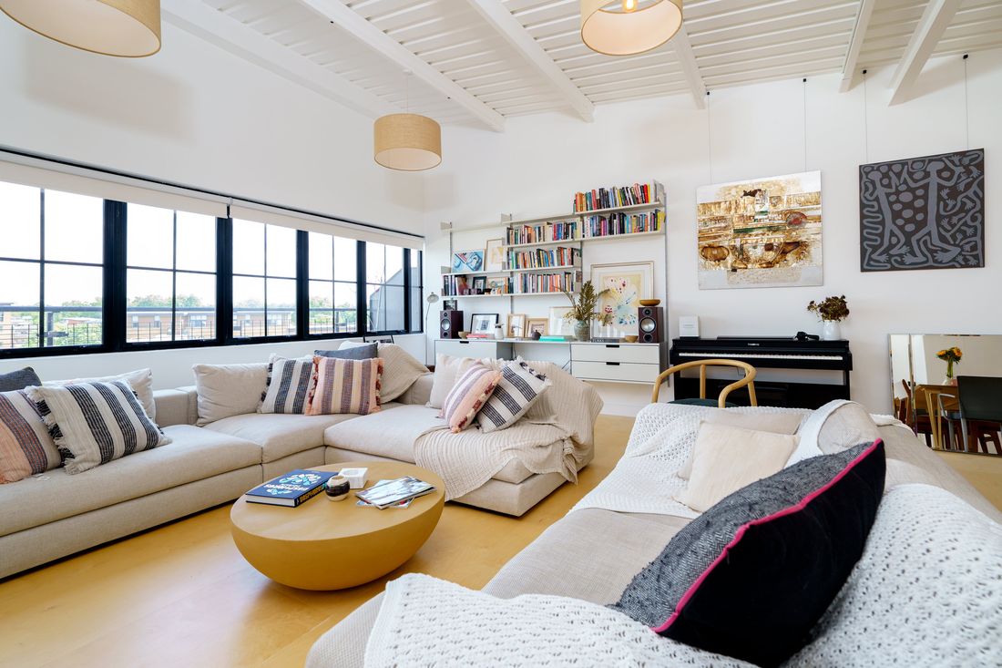 Open-plan warehouse loft living room with white beamed ceiling and steel-framed windows in Hackney